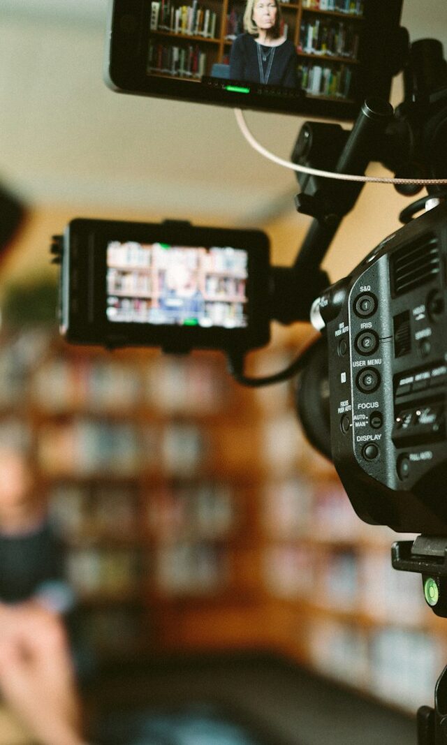 A broadcast camera and monitors rigged to film a seated interview in a library